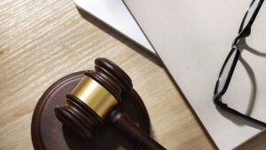 Martelo da justiça ao lado de documentos e óculos sobre uma mesa de madeira.
