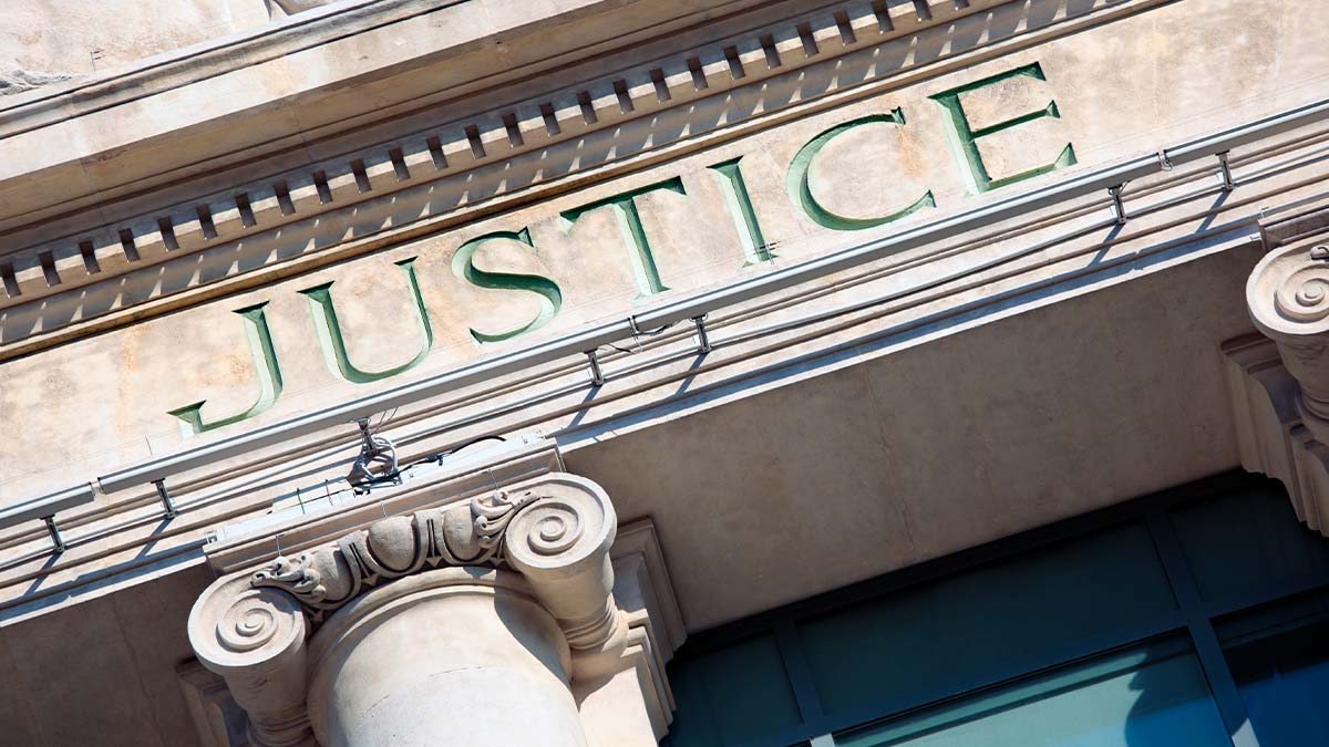 Fachada de tribunal com a palavra Justice esculpida, representando o conceito de diligência judicial vs extrajudicial