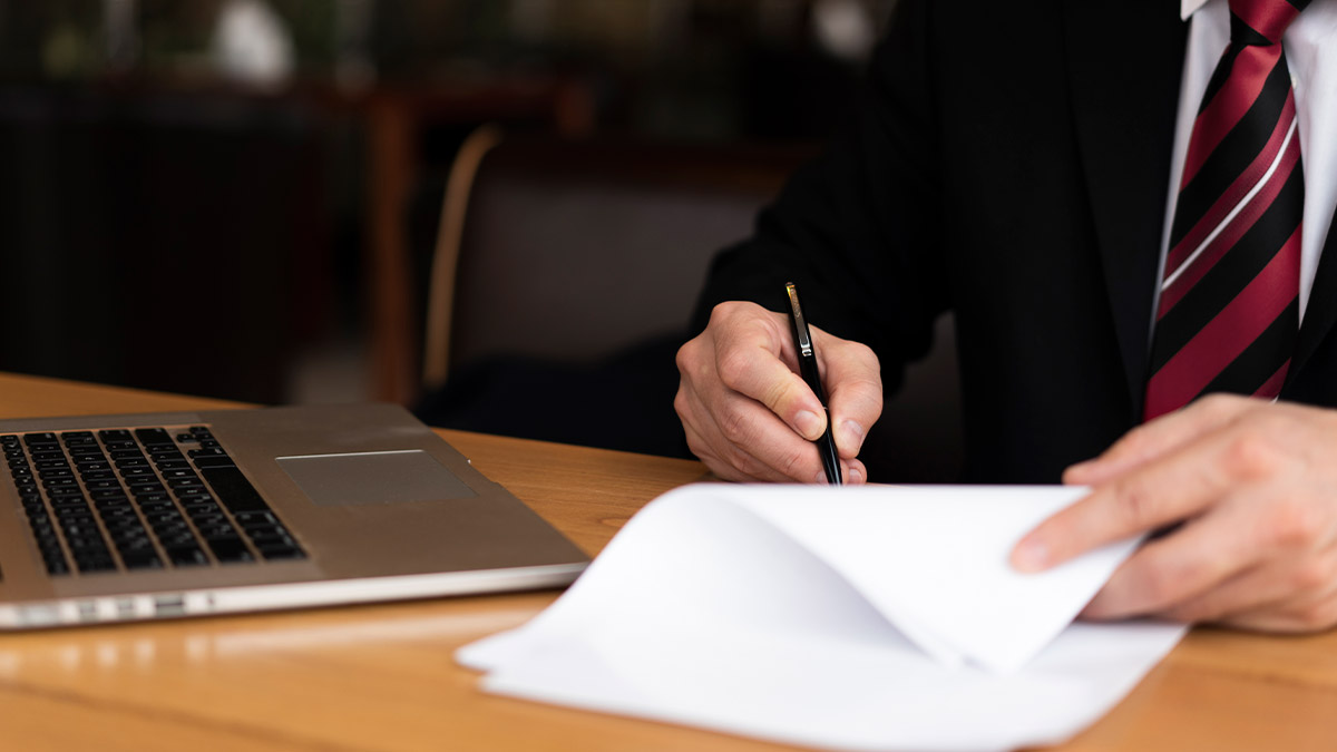 Advogado redigindo petição jurídica em mesa de escritório com laptop ao lado, representando criação de petição com inteligência artificial.