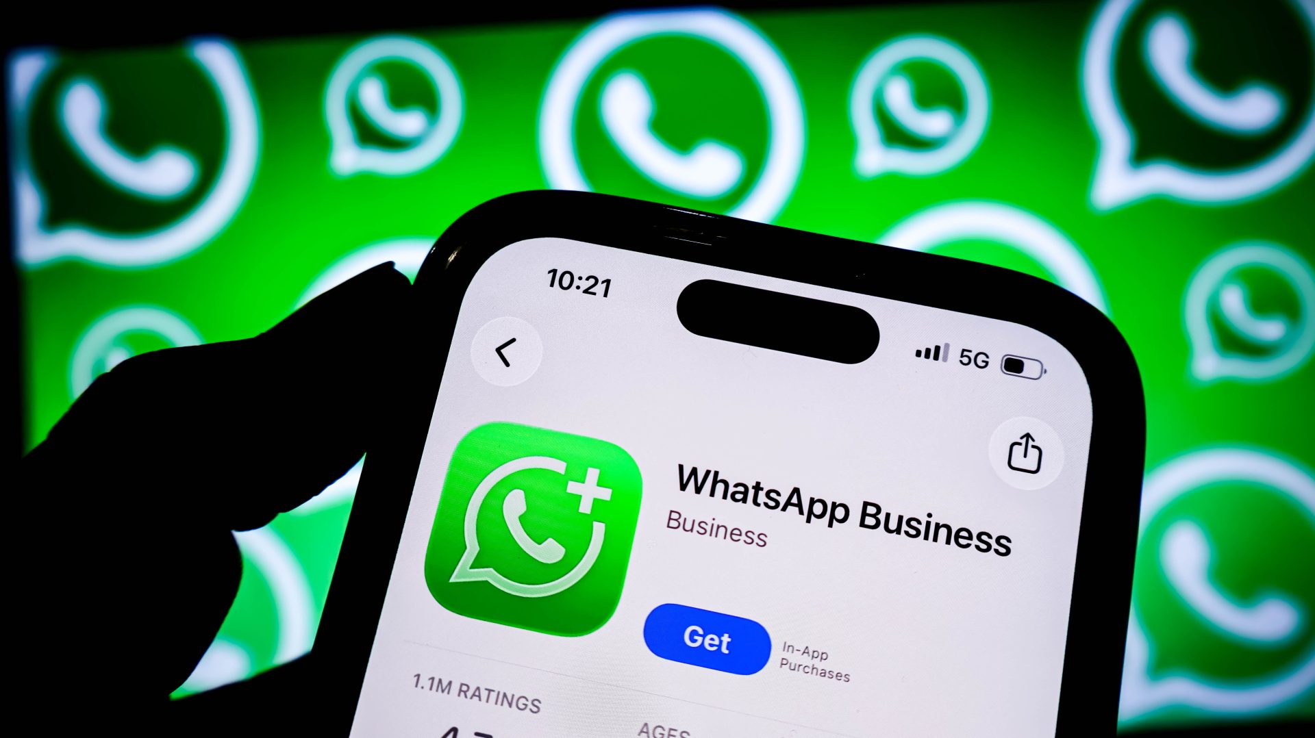 Mão segurando celular com a tela do aplicativo WhatsApp Business, com fundo de logotipos do WhatsApp